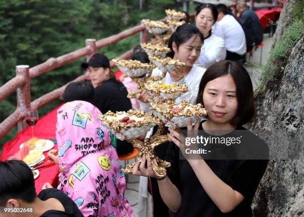 This photo taken on July 8, 2018 shows staff members serving food during a banquet held along the edge of a cliff, at Laojun Mountain in Luoyang in...