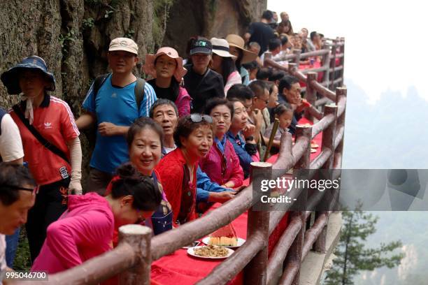 This photo taken on July 8, 2018 shows tourists during a banquet held along the edge of a cliff, at Laojun Mountain in Luoyang in China's central...