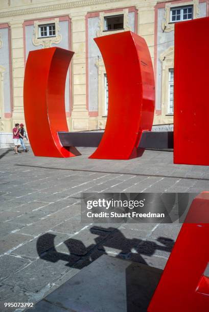 Two men walk past a piece of modernist art in the Piazza De Ferrari in Genoa, Italy. Situated in the heart of the city between the historical and the...
