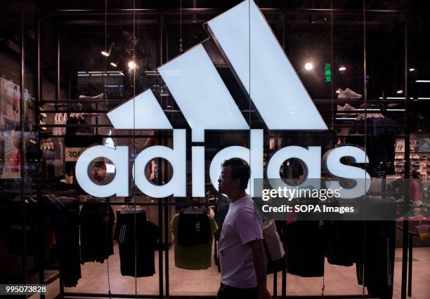 Pedestrian walks by a large Adidas logo and German multinational sportswear shop in Hong Kong.