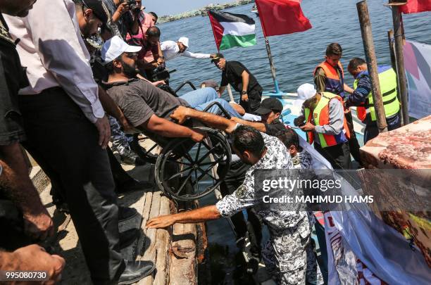 Members of Hamas' marine police help carry a wheelchaired-man onto a blockade-running boat carrying Palestinian students and others injured during...