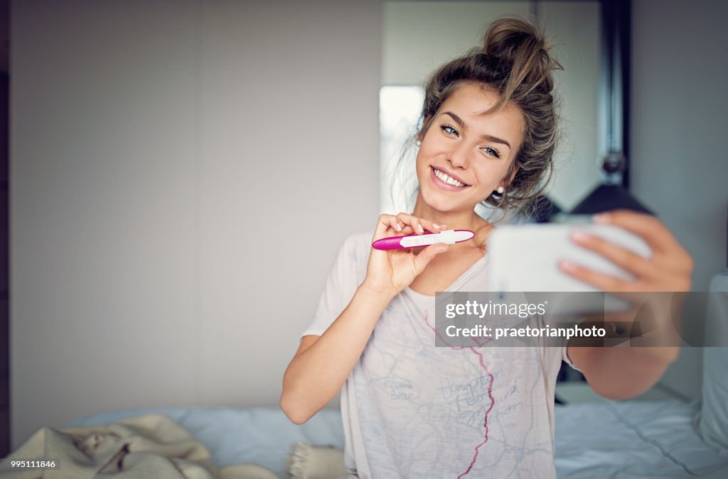 Glücklich, schwangere Mädchen zeigt ihr Schwangerschaftstest und nehmen Selfie/Making Videoanruf