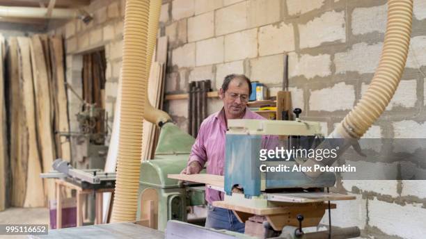 l'anziano di 60 anni, il falegname, che lavora con la rettificatrice industriale presso la piccola fabbrica di mobili - 55 years old foto e immagini stock