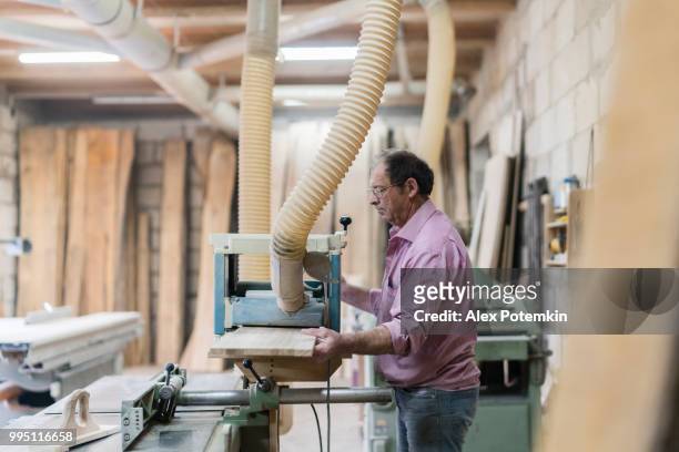 the senior 60-years-old man, the carpenter, working with the industrial grinding machine at the small furniture factory - alex potemkin or krakozawr stock pictures, royalty-free photos & images