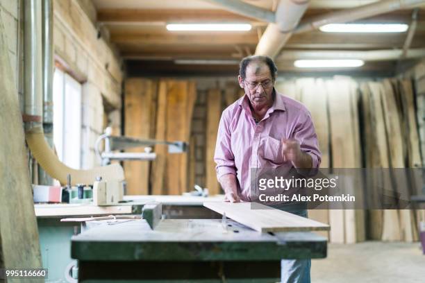 el mayor hombre de 60 años de edad, carpintero, trabajando con la máquina de sierra circular comercial en la fábrica de muebles pequeños - alex potemkin or krakozawr fotografías e imágenes de stock