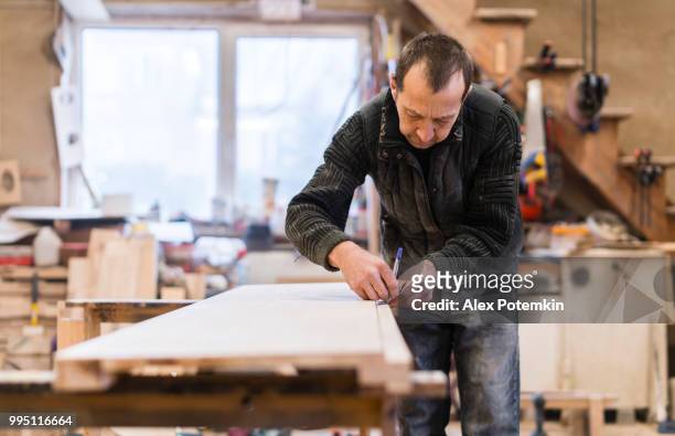 the senior man, carpenter, measuring and marking up a wooden detail for further processing. - alex potemkin or krakozawr stock pictures, royalty-free photos & images