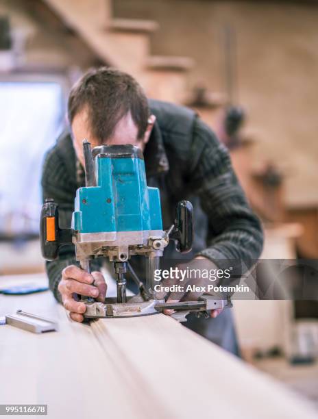 der senior 65 jährige handwerker arbeiten mit der elektrischen hand-fräsmaschine. holzarbeiten auf dem kleinen möbelfabrik. - alex potemkin or krakozawr stock-fotos und bilder