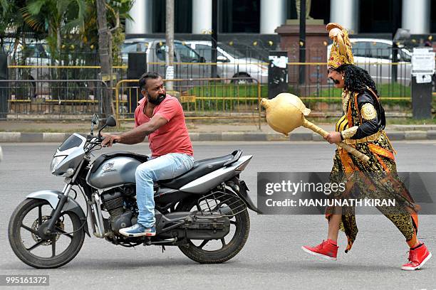 An artist dressed as "Yamaraj" , the Hindu god of death, runs behind a motorist riding without a helmet as part of a 'Road Safety Week' campaign...