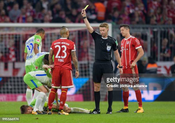 Referee Christian Dingert shows Bayern's Arturo Vidal the yellow card after his sliding tackle against Wolfsburg's Ignacio Camacho during the German...