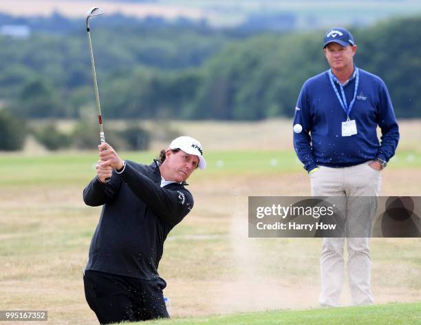 Phil Mickelson of the United States plays from the bunker in front of coach Andrew Gettison during practice for the Aberdeen Standard Investments...