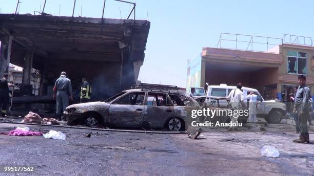 People inspect the scene near a wrecked car after a suicide bombing in Jalalabad in eastern Nanganhar province of Afghanistan on July 10, 2018....