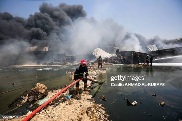 Iraqi firefighters attempt to put out a fire that broke out due to extreme summer temperatures in a warehouses near Palestine Street in the capital...