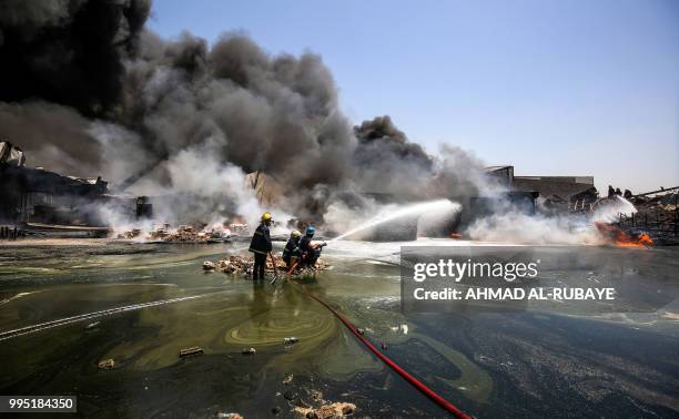 Iraqi firefighters attempt to put out a fire that broke out due to extreme summer temperatures in a warehouses near Palestine Street in the capital...