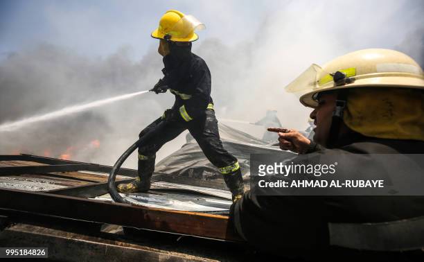 Iraqi firefighters attempt to put out a fire that broke out due to extreme summer temperatures in a warehouses near Palestine Street in the capital...