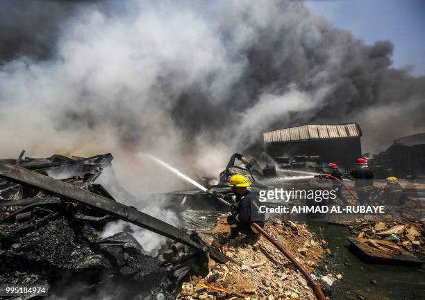 Iraqi firefighters attempt to put out a fire that broke out due to extreme summer temperatures in a warehouses near Palestine Street in the capital...