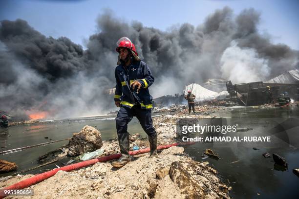 An Iraqi firefighter walks past a hose during a fire that broke out due to extreme summer temperatures in a warehouses near Palestine Street in the...