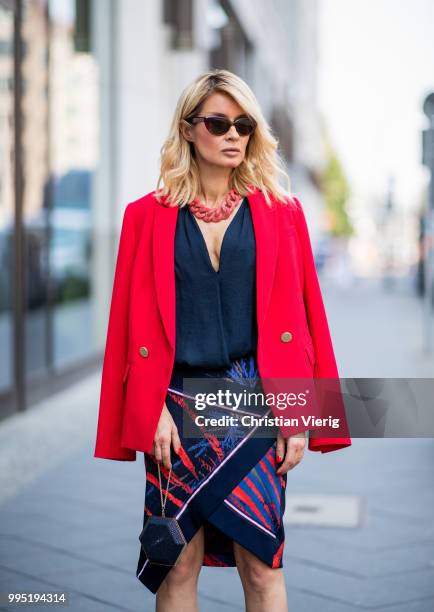 Gitta Banko wearing a red fitted blazer by Steffen Schraut, blue silk blouse with deep V-neck by Bash, red stingray leather oversize necklace by a...