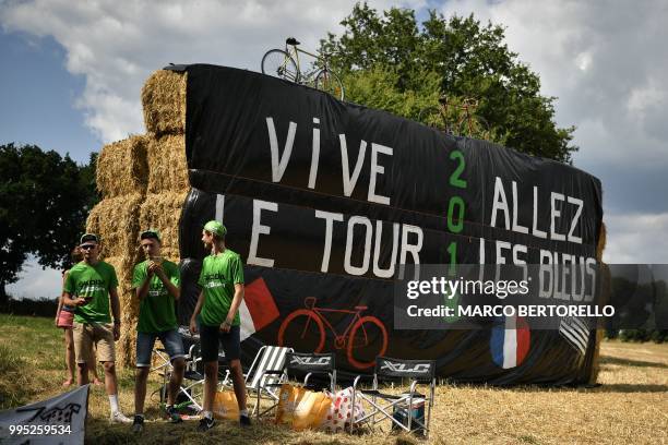 Young fans stand by haystacks with banners reading "Long live the Tour" and "Go the Blu Ones", referring to the French football team later competing...