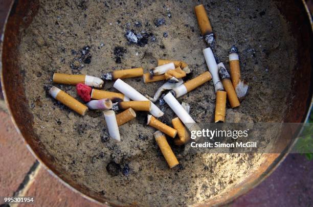 cigarette butts stubbed out in a metal bucket of sand - filtre de cigarette photos et images de collection