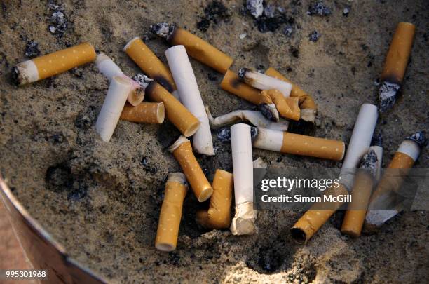 cigarette butts stubbed out in a metal bucket of sand - filtre de cigarette photos et images de collection