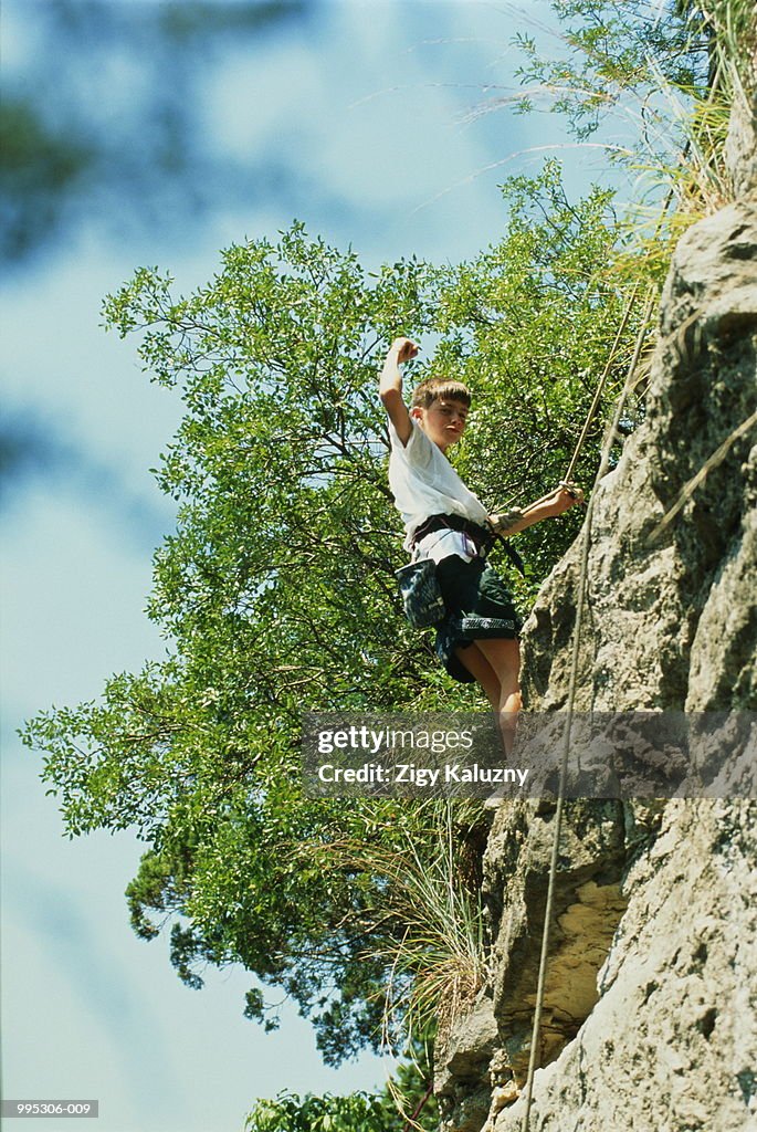 Boy (8-10) climbing up steep rock face