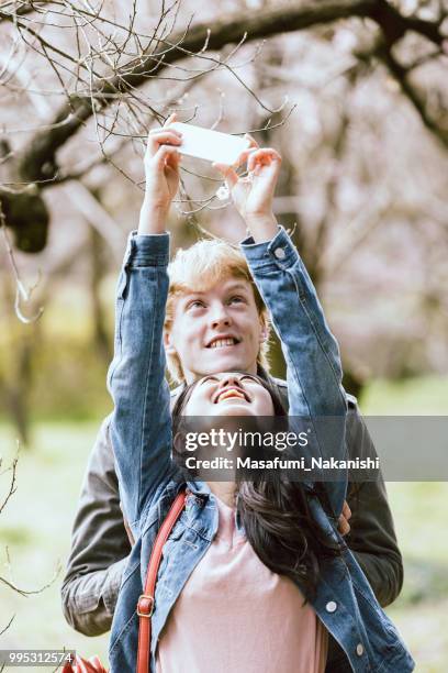 pareja de hombres blancos tiro flores de cerezo con teléfonos inteligentes y las mujeres asiáticas - masafumi nakanishi fotografías e imágenes de stock