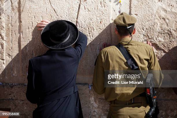 an israeli soldier and an ultra orthodox jewish man pray at the western wall - ultra foto e immagini stock