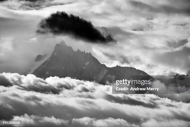 aiguille du midi summit, peak, mountain range appearing above the clouds with large dark cloud - sallanches stockfoto's en -beelden