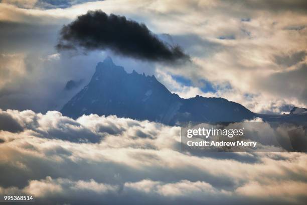 aiguille du midi summit, peak, mountain range appearing above the clouds with large dark cloud - sallanches stockfoto's en -beelden