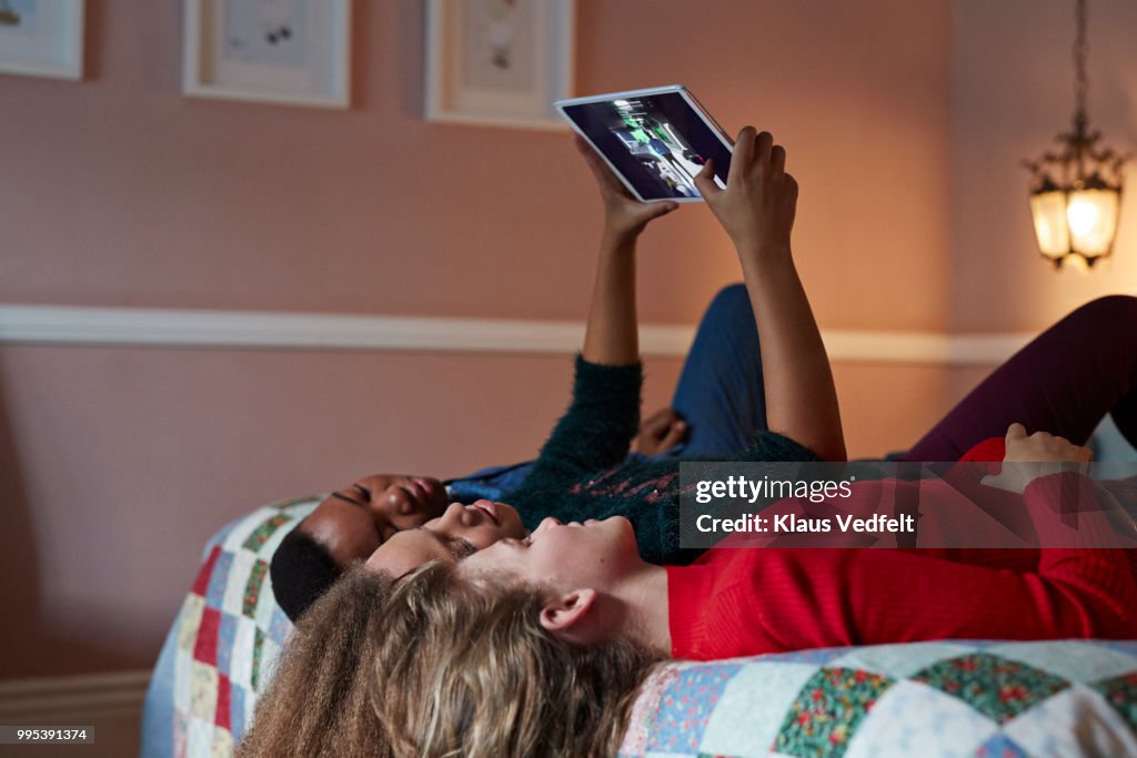 Friends laying in bed and looking at tablet with pictures