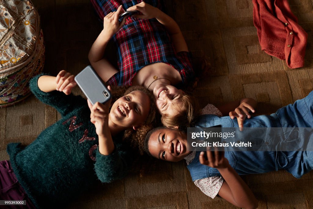 Top view of 3 tween girls laughing and looking at their smartphones