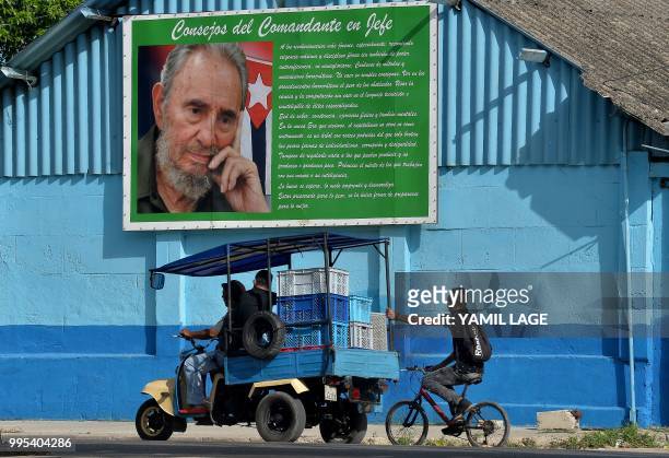 Workers transport goods for sale past a poster of Cuban late leader Fidel Castro in Havana, on June 10, 2018. - Cuba gave Tuesday a new green light...