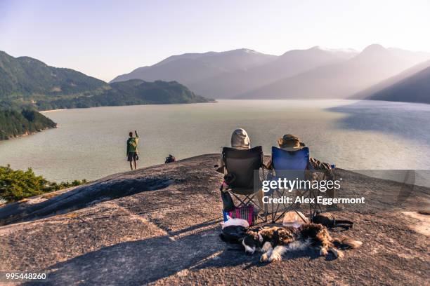 friends relaxing in camping chairs on mountain ledge overlooking lake, squamish, canada - camping chair stock pictures, royalty-free photos & images