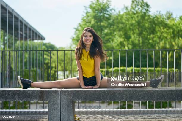 portrait of smiling young woman doing splits on bench outdoors - slide tackle stock pictures, royalty-free photos & images