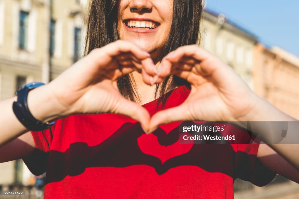 Woman's hands shaping heart, shadow on red t-shirt