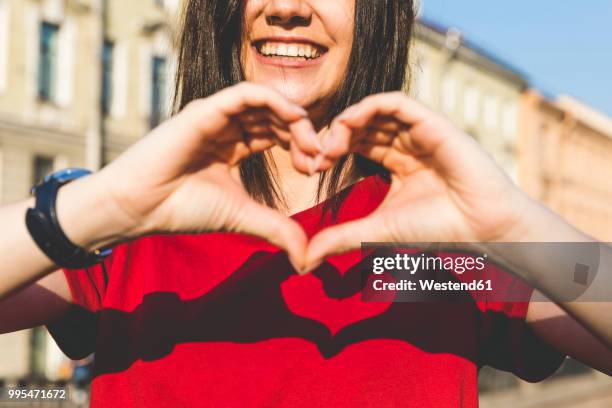 woman's hands shaping heart, shadow on red t-shirt - red t shirt stock pictures, royalty-free photos & images