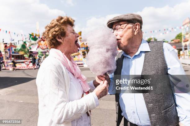 senior couple on fair eating together cotton candy - fun stock-fotos und bilder