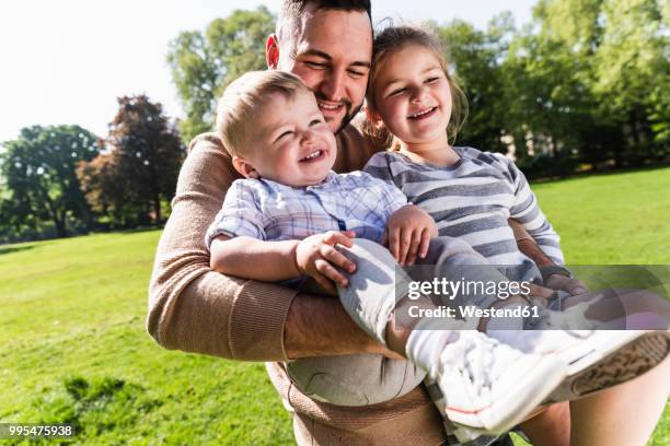 happy father carrying children in a park - beschützer stock-fotos und bilder