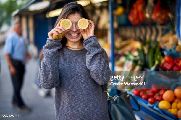 laughing young woman on market covering her eyes with lemon halves - market retail space stock pictures, royalty-free photos & images