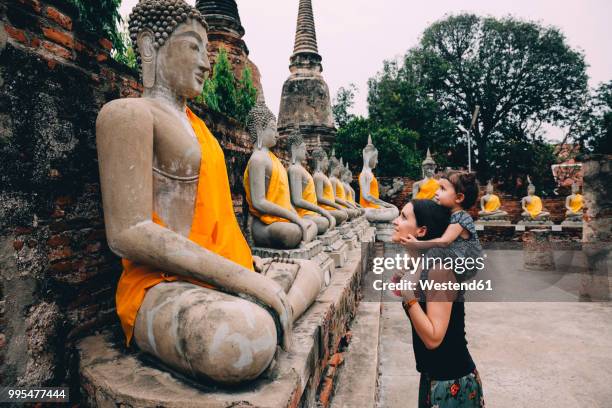 thailand, bangkok, ayutthaya, buddha statues in a row in wat yai chai mongkhon, mother and daughter in front of a buddha statue - thailand stock-fotos und bilder