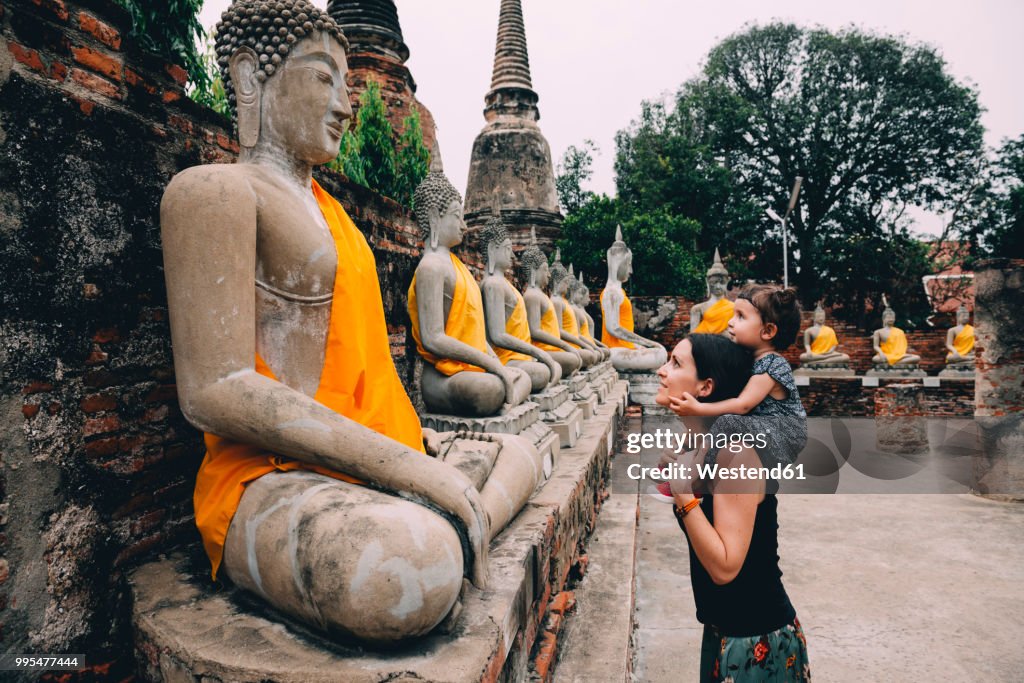 Thailand, Bangkok, Ayutthaya, Buddha statues in a row in Wat Yai Chai Mongkhon, mother and daughter in front of a buddha statue