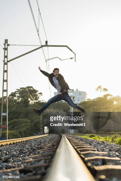young man jumping into the air, railroad track - mann freudensprung sonne vorderansicht leger stock-fotos und bilder