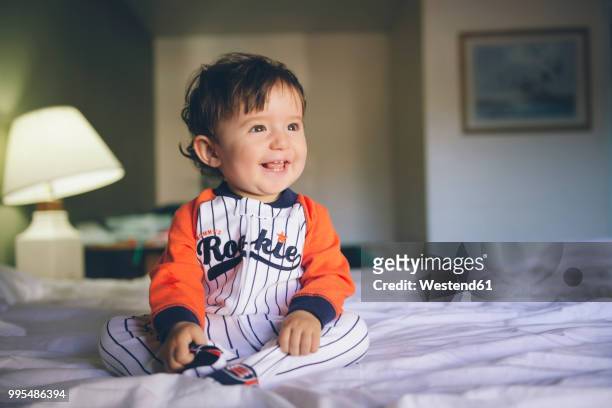 portrait of laughing baby girl wearing jumpsuit sitting on bed - one baby girl only stock pictures, royalty-free photos & images