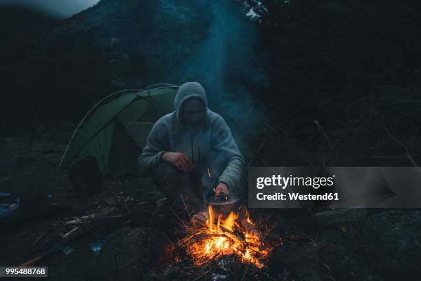 norway, lofoten, moskenesoy, young man sitting at camp fire - moskenesoya stock pictures, royalty-free photos & images