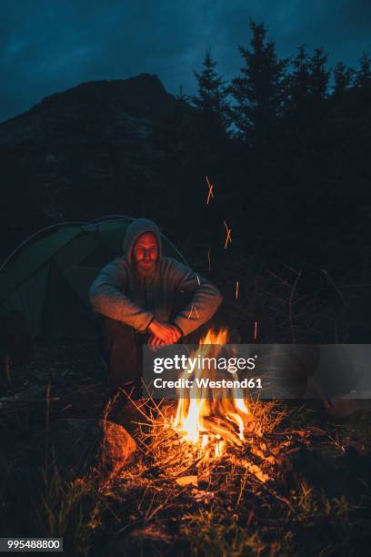 norway, lofoten, moskenesoy, young man sitting at camp fire - moskenesoya stock pictures, royalty-free photos & images