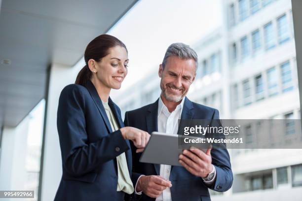 portrait of two business partners looking together at tablet - blue blazer stock pictures, royalty-free photos & images