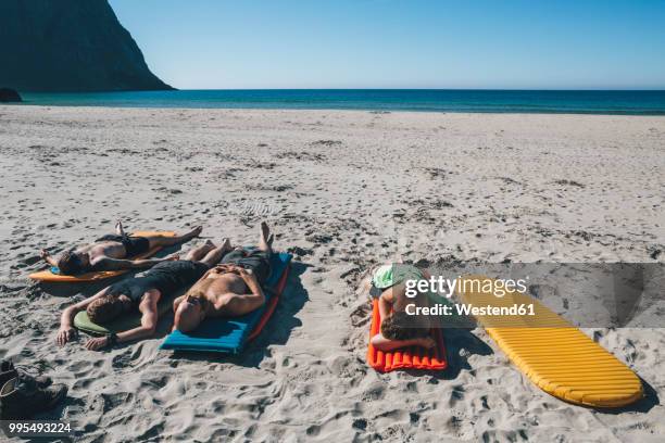 norway, lofoten, moskenesoy, friends sunbathing on kvalvika beach - moskenesoya stock pictures, royalty-free photos & images
