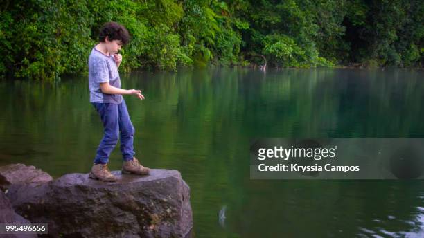 boy throwing rock into lagoon at rainforest - alajuela stockfoto's en -beelden