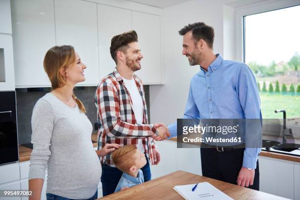 family and real estate agent shaking hands in kitchen of new apartment - ethnic millennial real estate stockfoto's en -beelden