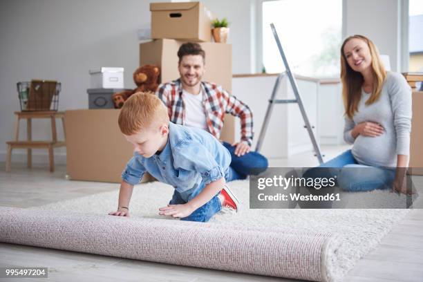 boy with parents unrolling a carpet in new flat - perfect home stock pictures, royalty-free photos & images